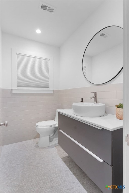 bathroom featuring tile patterned flooring, vanity, toilet, and tile walls