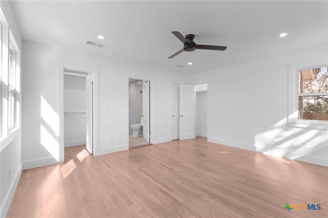 unfurnished bedroom with a walk in closet, light hardwood / wood-style flooring, ensuite bath, ceiling fan, and a closet