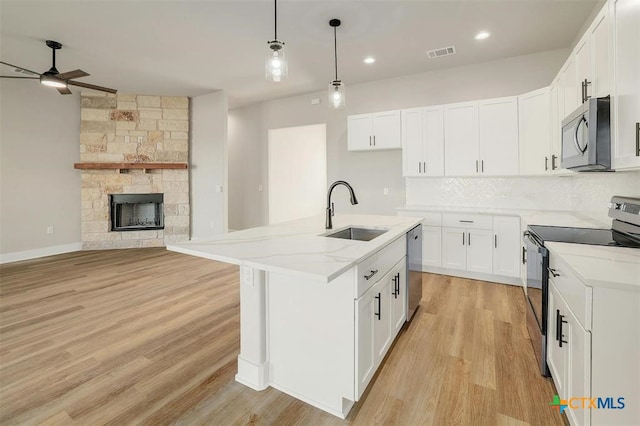 kitchen with appliances with stainless steel finishes, sink, decorative light fixtures, white cabinetry, and an island with sink