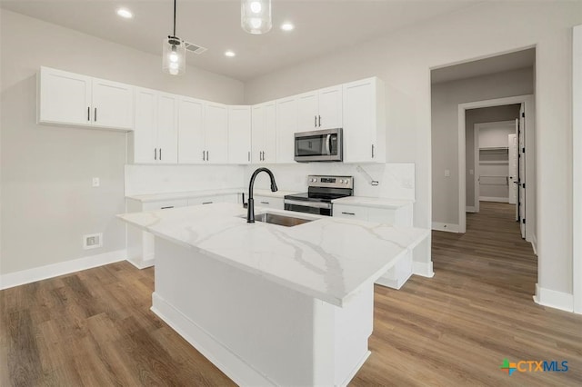 kitchen featuring a kitchen island with sink, white cabinets, light stone counters, and appliances with stainless steel finishes