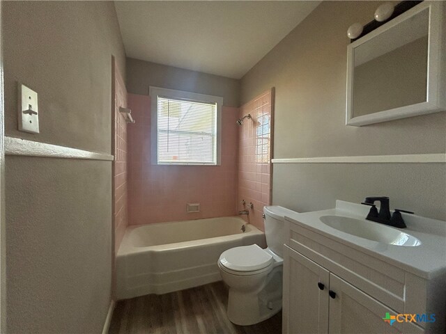 full bathroom with tiled shower / bath combo, vanity, hardwood / wood-style flooring, and toilet