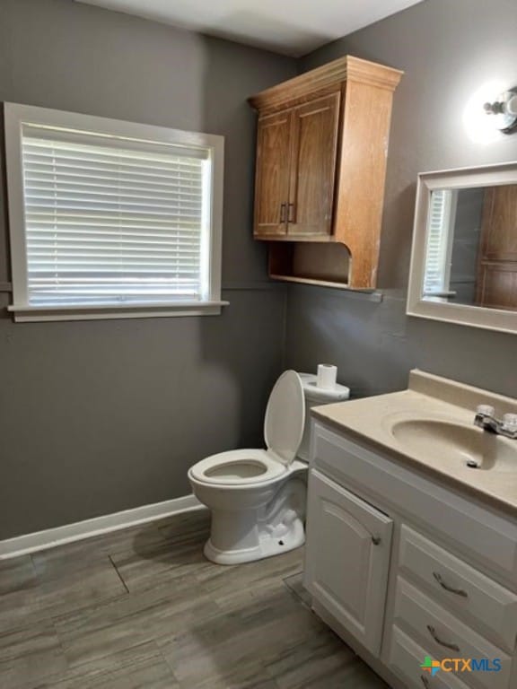 half bathroom featuring baseboards, toilet, wood finished floors, and vanity