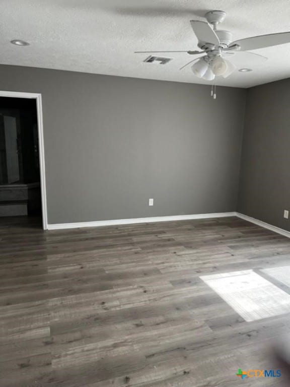 empty room featuring a textured ceiling, wood finished floors, baseboards, and ceiling fan