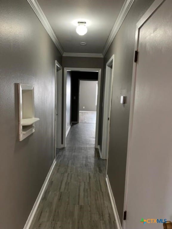 hall featuring dark wood-type flooring, baseboards, and ornamental molding