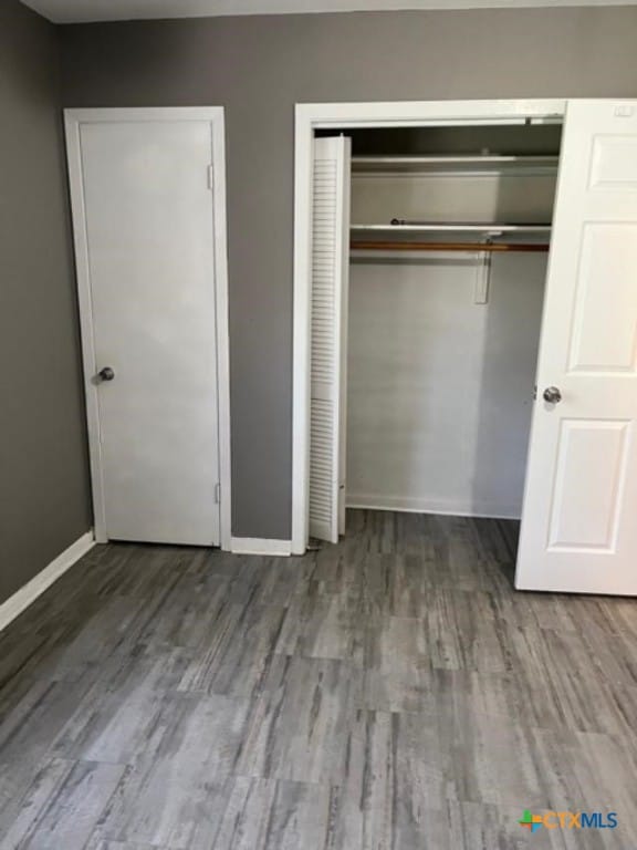 unfurnished bedroom featuring a closet, baseboards, and wood finished floors