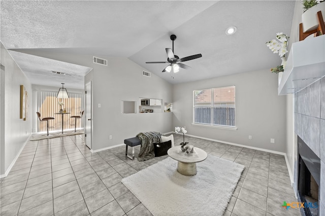 tiled living room with a textured ceiling, a tile fireplace, ceiling fan, and lofted ceiling