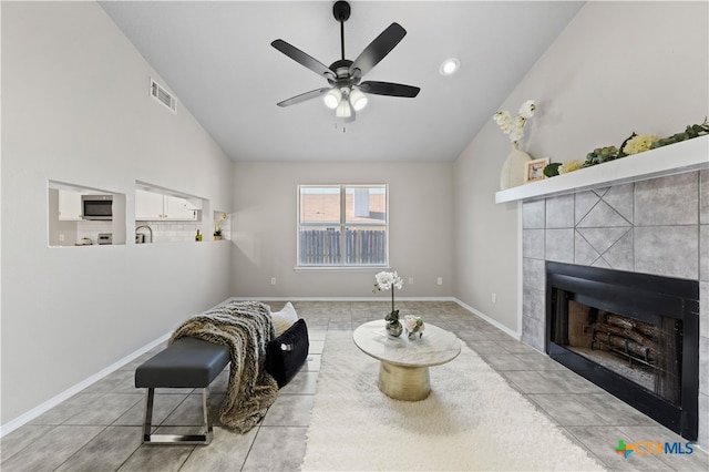 living area featuring ceiling fan, vaulted ceiling, light tile patterned floors, and a tiled fireplace