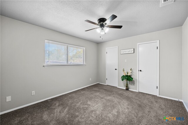 unfurnished bedroom with ceiling fan, dark carpet, and a textured ceiling