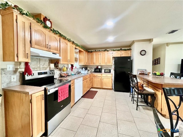 kitchen with under cabinet range hood, black appliances, light brown cabinetry, light tile patterned floors, and light countertops