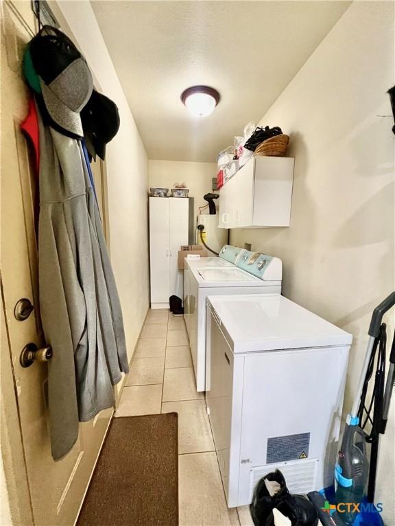 washroom featuring cabinet space, washing machine and clothes dryer, and light tile patterned floors