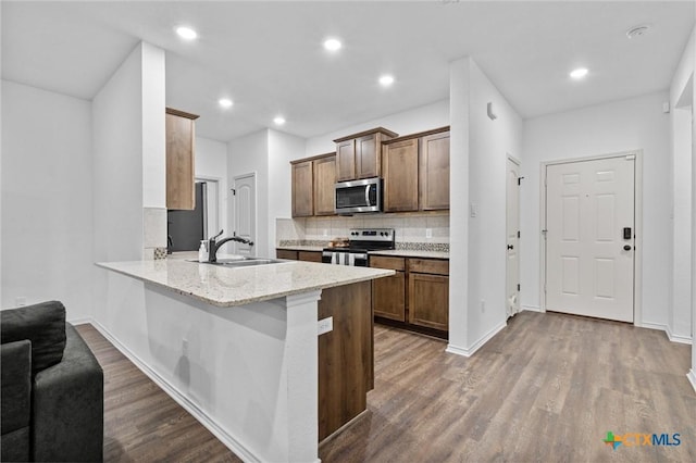 kitchen featuring tasteful backsplash, kitchen peninsula, sink, hardwood / wood-style flooring, and stainless steel appliances