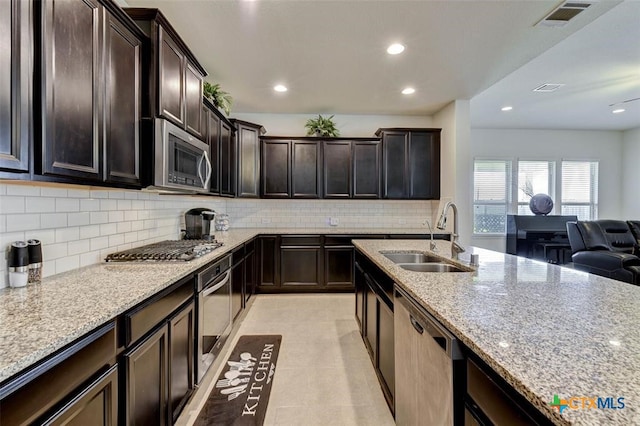 kitchen featuring stainless steel appliances, backsplash, dark brown cabinets, light stone countertops, and sink