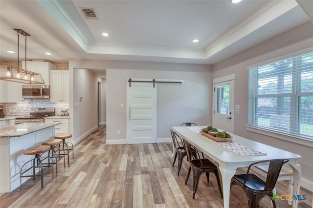 dining room featuring light hardwood / wood-style flooring, ornamental molding, a barn door, and a raised ceiling