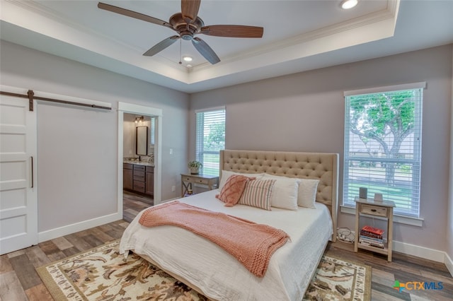 bedroom featuring hardwood / wood-style floors, ornamental molding, a barn door, and a raised ceiling