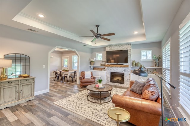 living room featuring a fireplace, ceiling fan, a raised ceiling, crown molding, and light hardwood / wood-style flooring