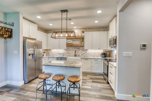 kitchen with a kitchen island, appliances with stainless steel finishes, white cabinetry, sink, and a breakfast bar area