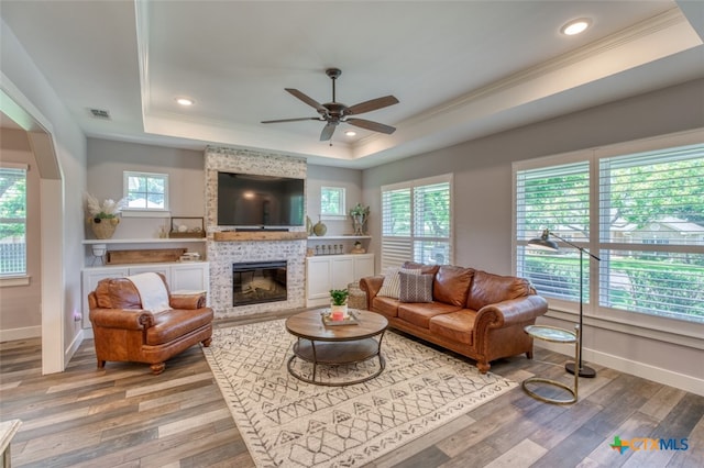 living room with a tiled fireplace, hardwood / wood-style flooring, a raised ceiling, and ceiling fan