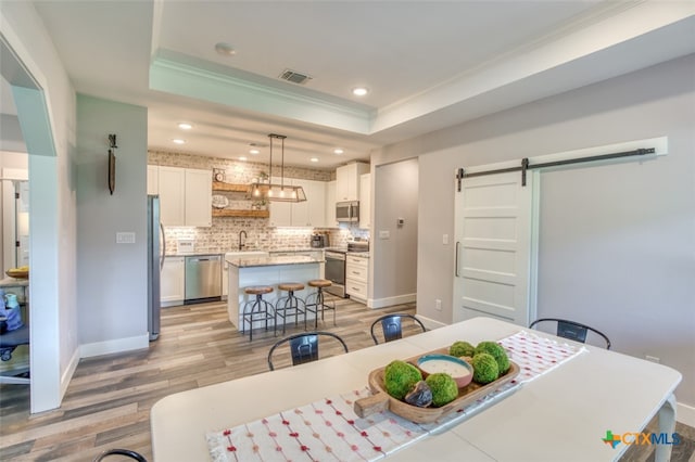 dining area with sink, crown molding, a tray ceiling, a barn door, and light hardwood / wood-style floors