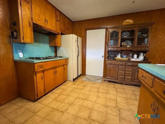 2410 Robin Rd, Temple, TX 76502 - kitchen with under cabinet range hood, brown cabinets, gas cooktop, wooden walls, and a textured ceiling