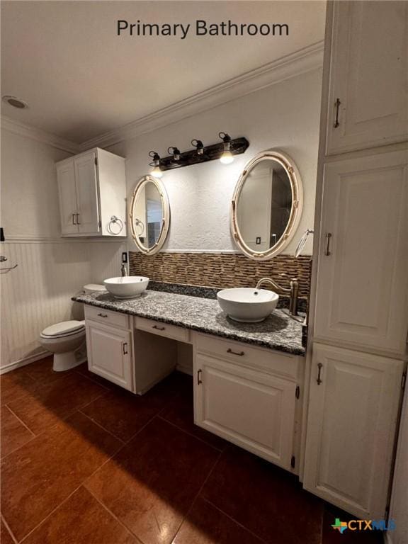 bathroom featuring a sink, backsplash, toilet, and double vanity