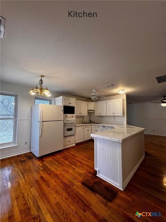 kitchen featuring white appliances, visible vents, dark wood finished floors, white cabinets, and a peninsula