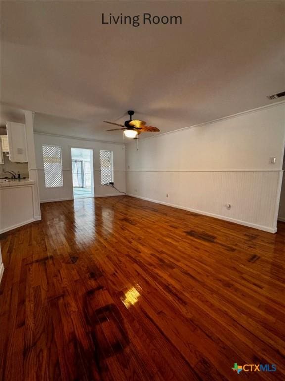 unfurnished living room featuring visible vents, dark wood finished floors, a ceiling fan, and wainscoting