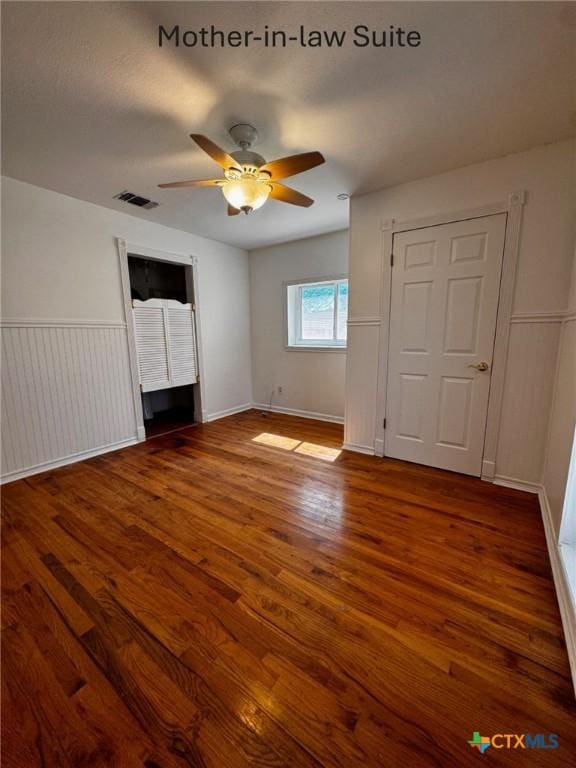 unfurnished bedroom featuring ceiling fan, wainscoting, wood finished floors, and visible vents