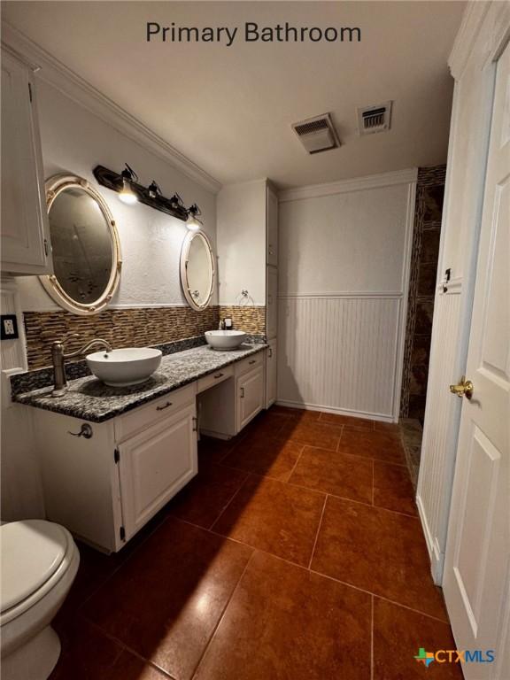 full bathroom featuring double vanity, visible vents, crown molding, and wainscoting