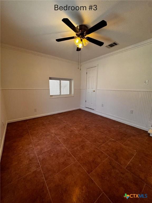 unfurnished room featuring ornamental molding, dark tile patterned flooring, wainscoting, and visible vents