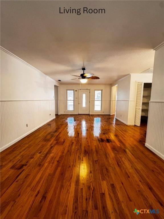 unfurnished living room featuring ornamental molding, wainscoting, wood finished floors, and a ceiling fan