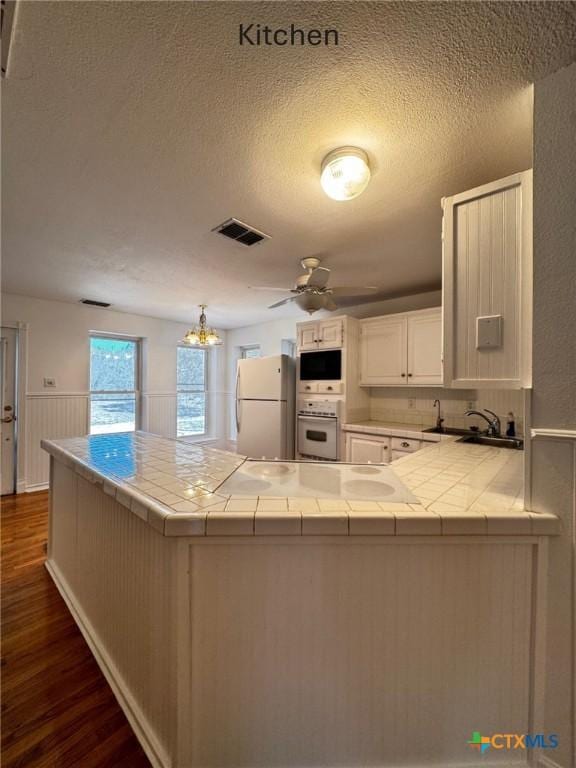 kitchen with tile countertops, a peninsula, white appliances, visible vents, and dark wood finished floors