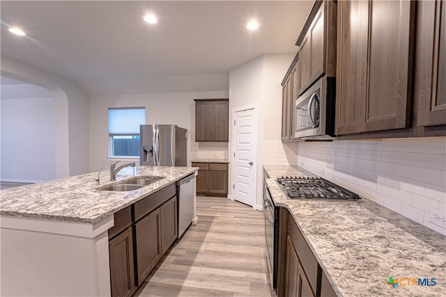 kitchen with a center island with sink, stainless steel appliances, decorative backsplash, sink, and light hardwood / wood-style flooring