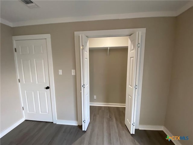 unfurnished bedroom featuring dark wood-style floors, baseboards, visible vents, and crown molding