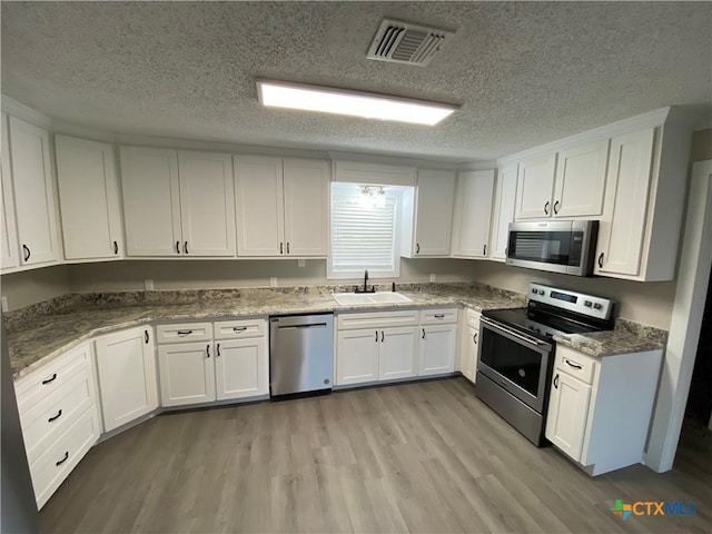 kitchen with appliances with stainless steel finishes, white cabinets, visible vents, and a sink