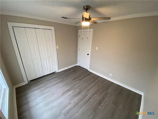 unfurnished bedroom with baseboards, visible vents, dark wood-style floors, a textured ceiling, and a closet