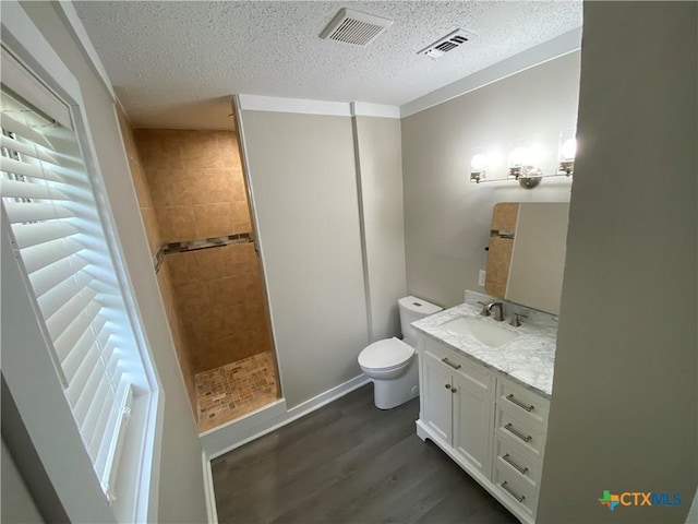 full bath featuring vanity, wood finished floors, a tile shower, and visible vents