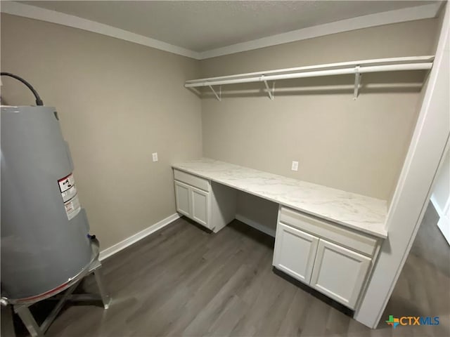 unfurnished office featuring baseboards, built in study area, dark wood-style floors, crown molding, and water heater