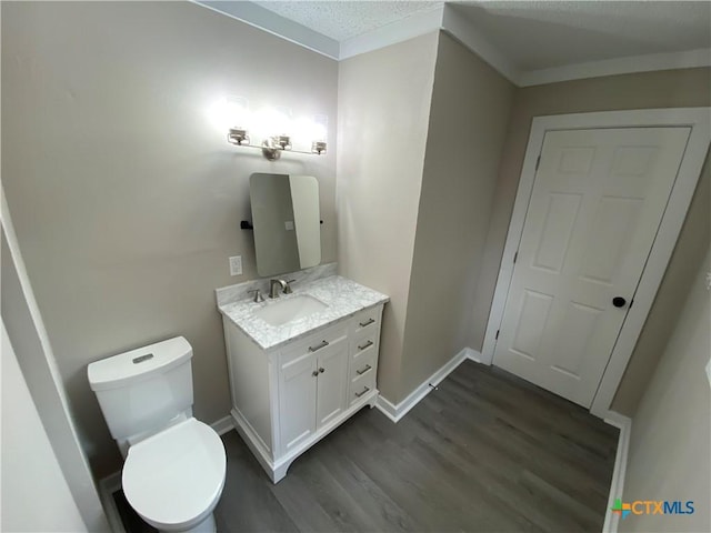 half bathroom with toilet, a textured ceiling, vanity, wood finished floors, and baseboards