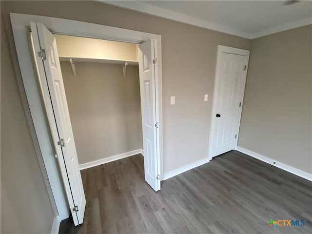 unfurnished bedroom featuring dark wood-type flooring, a closet, crown molding, and baseboards