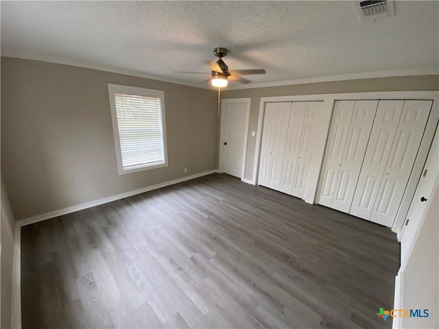 unfurnished bedroom featuring a textured ceiling, dark wood finished floors, visible vents, baseboards, and two closets