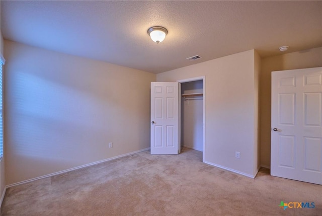 unfurnished bedroom with light carpet, a textured ceiling, and a closet