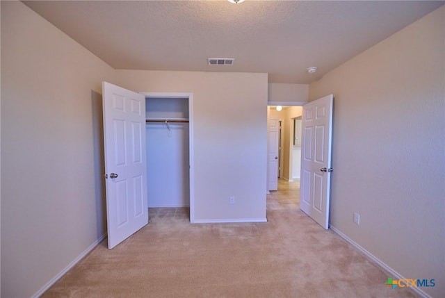 unfurnished bedroom featuring light colored carpet, a textured ceiling, and a closet