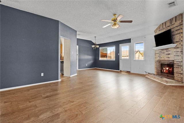 unfurnished living room featuring a textured ceiling, ceiling fan with notable chandelier, a fireplace, and hardwood / wood-style floors