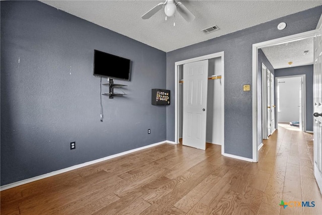 unfurnished bedroom featuring ceiling fan, light wood-type flooring, a closet, and a textured ceiling