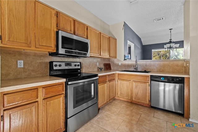 kitchen with pendant lighting, appliances with stainless steel finishes, sink, a chandelier, and light tile patterned floors