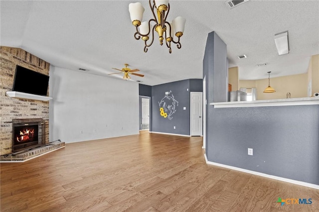 unfurnished living room featuring a brick fireplace, a textured ceiling, hardwood / wood-style flooring, and ceiling fan with notable chandelier