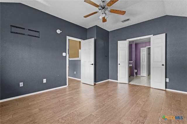 unfurnished bedroom with ceiling fan, light hardwood / wood-style flooring, ensuite bath, and lofted ceiling