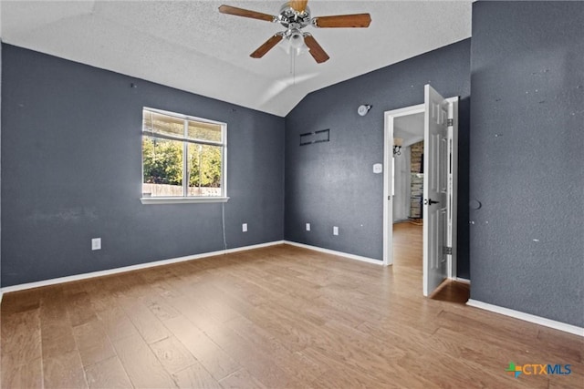 empty room with vaulted ceiling, ceiling fan, a textured ceiling, and hardwood / wood-style floors