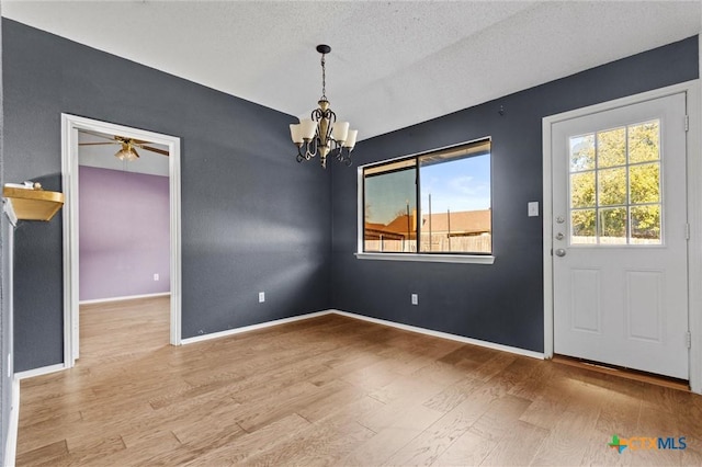 unfurnished dining area featuring light wood-type flooring, a textured ceiling, and ceiling fan with notable chandelier