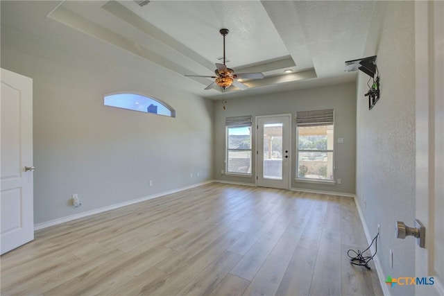 empty room with ceiling fan, a tray ceiling, and light wood-type flooring